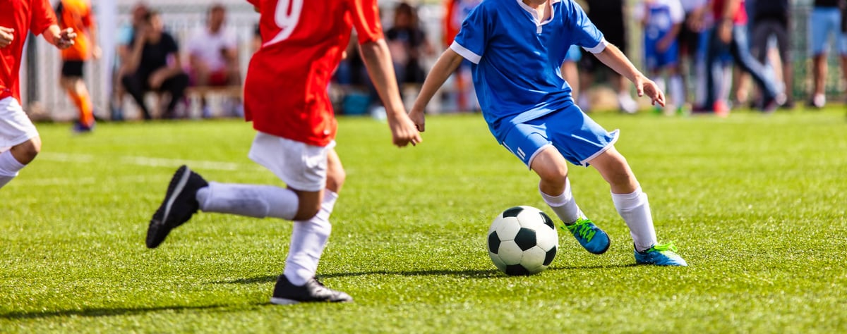 Teenagers playing competitive soccer in sports field, young male footballers running in red and blue uniforms during an active match